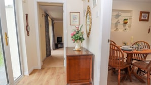 A hallway leading to a dining area with a wooden table and chairs, a vase with flowers, and a mirror on the wall. - Bryn Offa Cottage (Holywell)