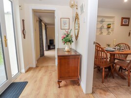 A hallway leading to a dining area with a wooden table and chairs, a vase with flowers, and a mirror on the wall.
