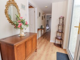 A hallway with a wooden cabinet, a mirror, a vase with flowers, a small table, and a shelf with decorative items.
