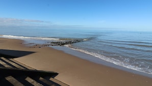 A beach with a clear sky, calm sea, and a rocky outcrop near the shore. - Bryn Offa Cottage (Holywell)