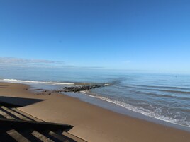 A beach with a clear sky, calm sea, and a rocky outcrop near the shore.