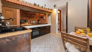 A kitchen with a brick oven, wooden cabinets, a sink, and a dining area with a table set for two. - Villa Stone House Magarac (Starigrad)