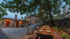 An outdoor dining area with a stone patio, wooden furniture, and a stone building in the background. - Villa Stone House Magarac (Starigrad)