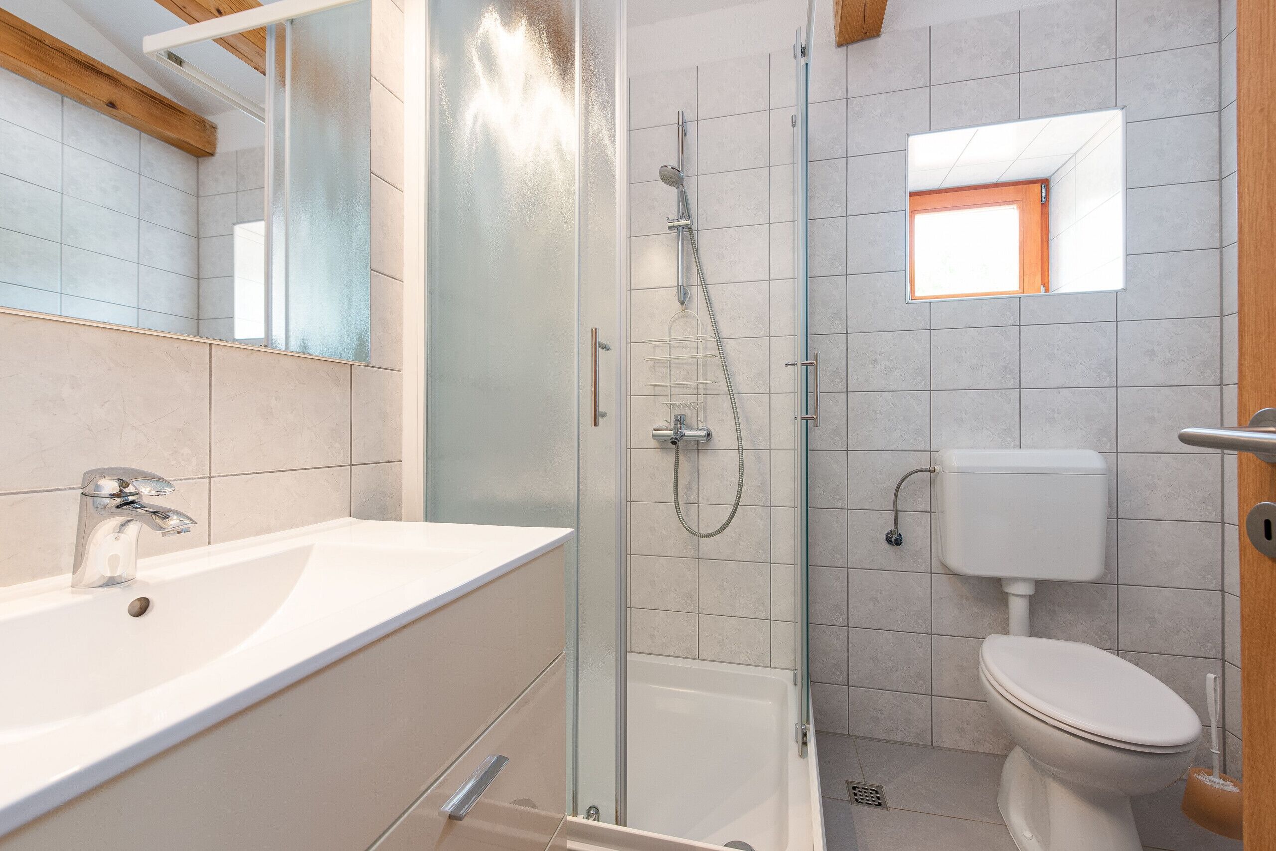 Et moderne badeværelse med en glasafskærmet brusekabine, en hvid vask og et toilet.
