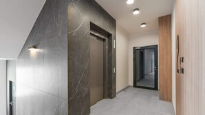 A modern elevator with a marble wall, a wooden panel, and a glass door.
