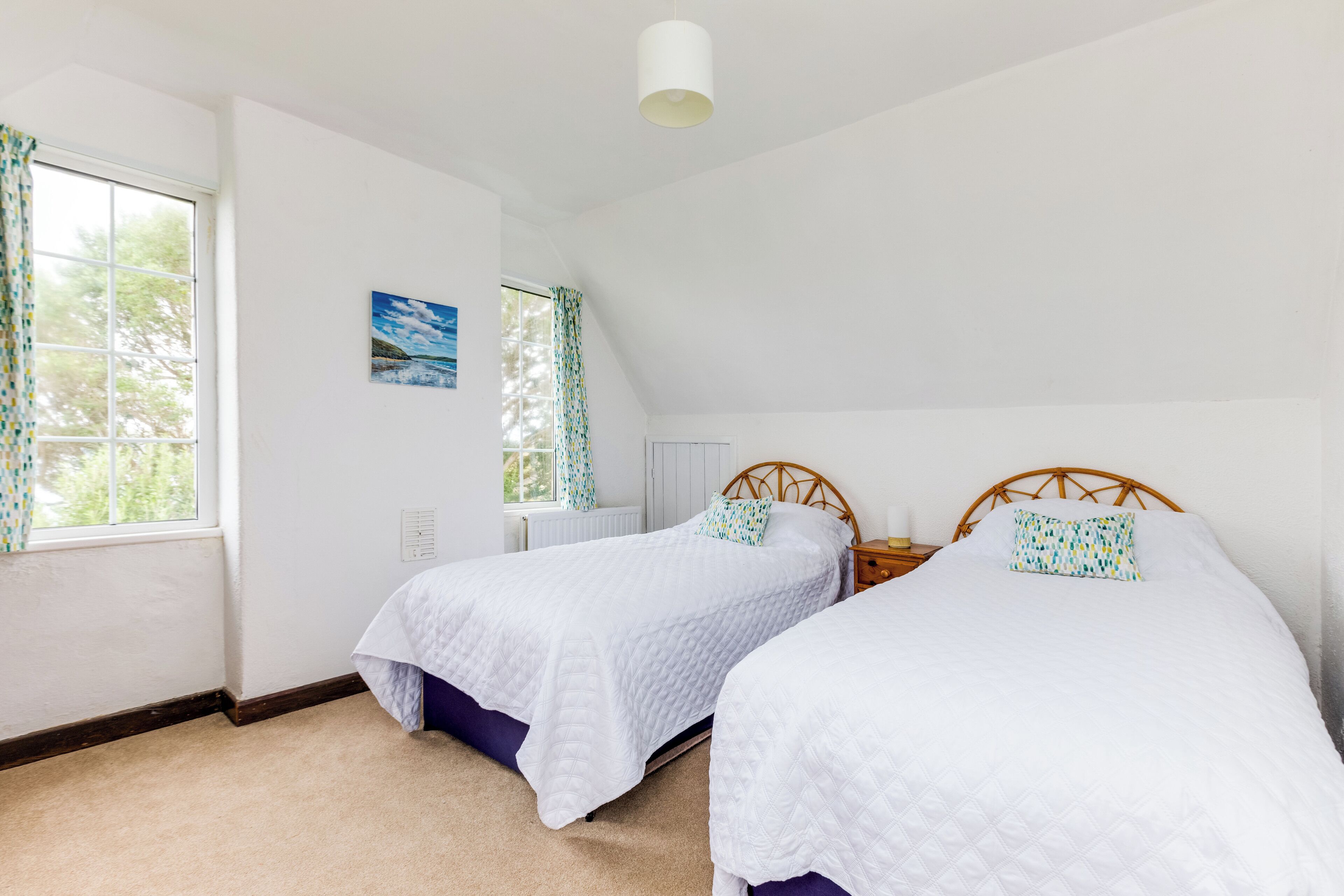 A bedroom with two single beds, a window with curtains, a painting on the wall, and a ceiling light.
