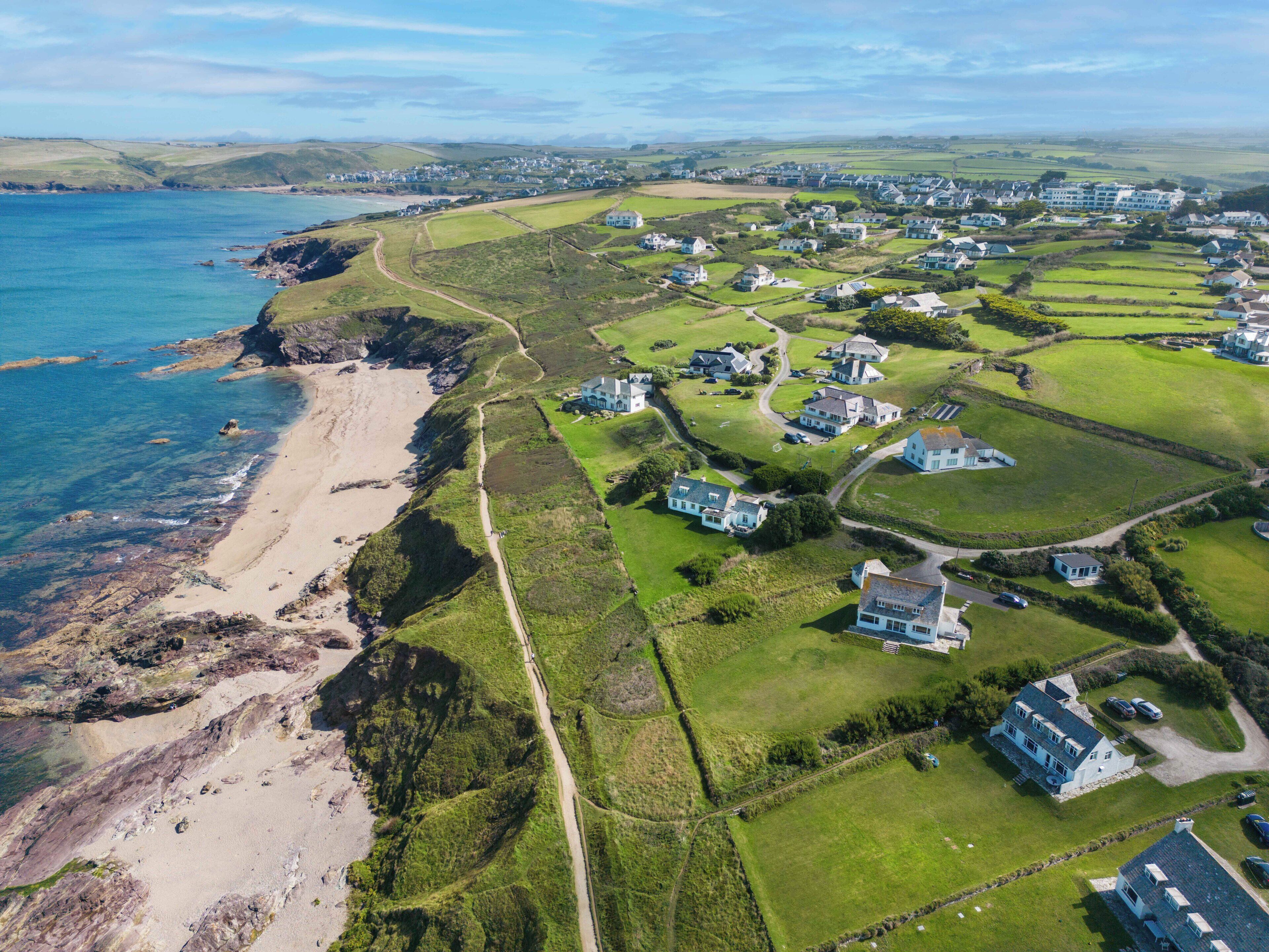 An aerial view of a coastal residential area with houses, a beach, and a clear sky.