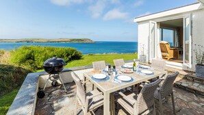 Un área de comedor al aire libre con vista al mar, una parrilla, sillas de mimbre y una mesa preparada para dos.