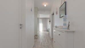 A hallway with a wooden floor, white walls, and a white dresser with drawers and a mirror.