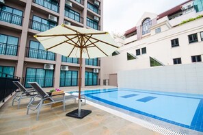 A swimming pool with lounge chairs and an umbrella, surrounded by a building with balconies and air conditioning units. - Marsi Hotel Bangchak (Bangkok)