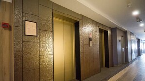 Um corredor com elevadores e portas, um aviso na parede e um painel de alarme de incêndio.
