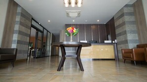 Uma área de recepção com design moderno, com um balcão de atendimento, uma mesa redonda com um vaso de flores e uma área de estar com poltronas de couro.