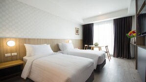 Quarto de hotel com duas camas, uma escrivaninha, uma cadeira, uma televisão e uma janela com cortinas.