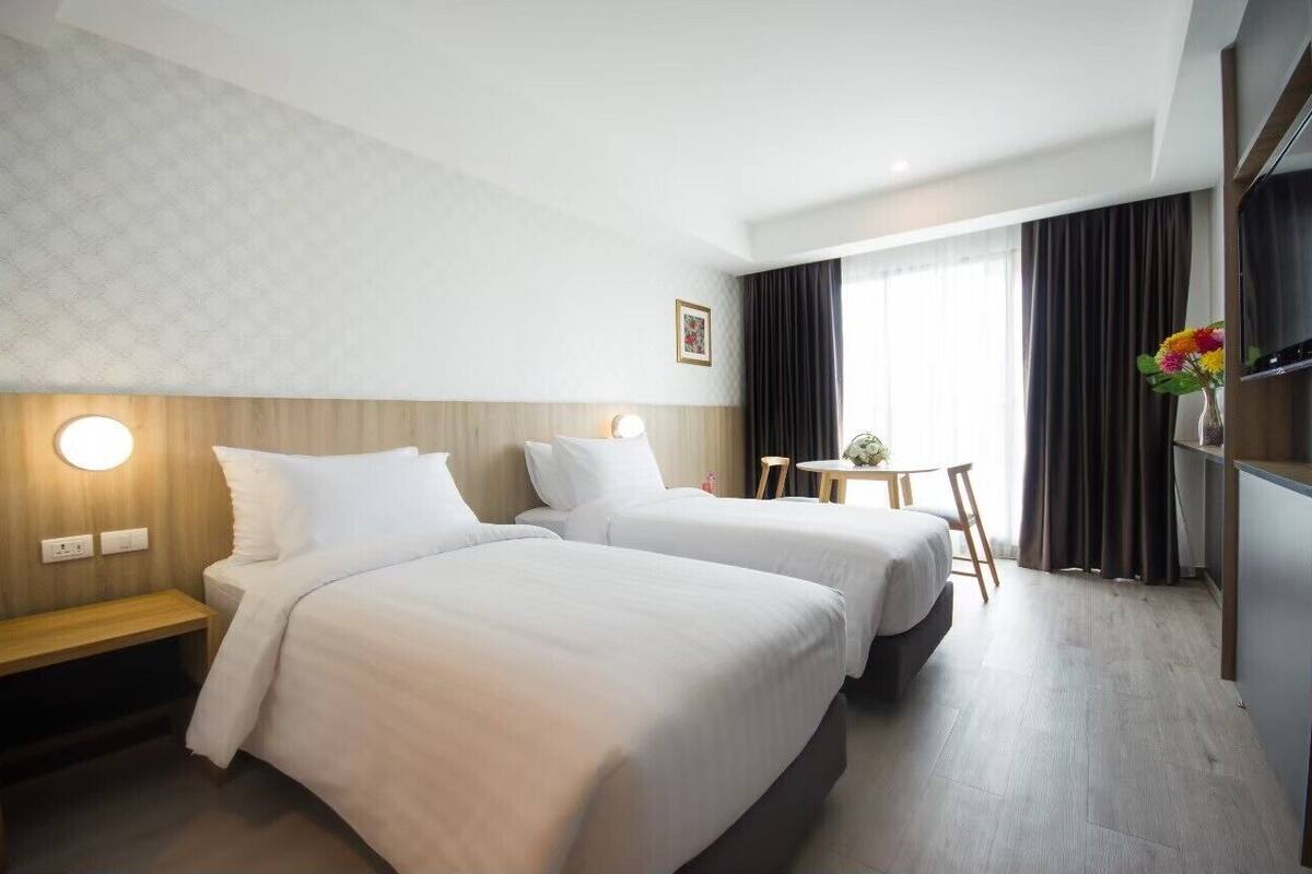 Quarto de hotel com duas camas, uma escrivaninha, uma cadeira, uma televisão e uma janela com cortinas.