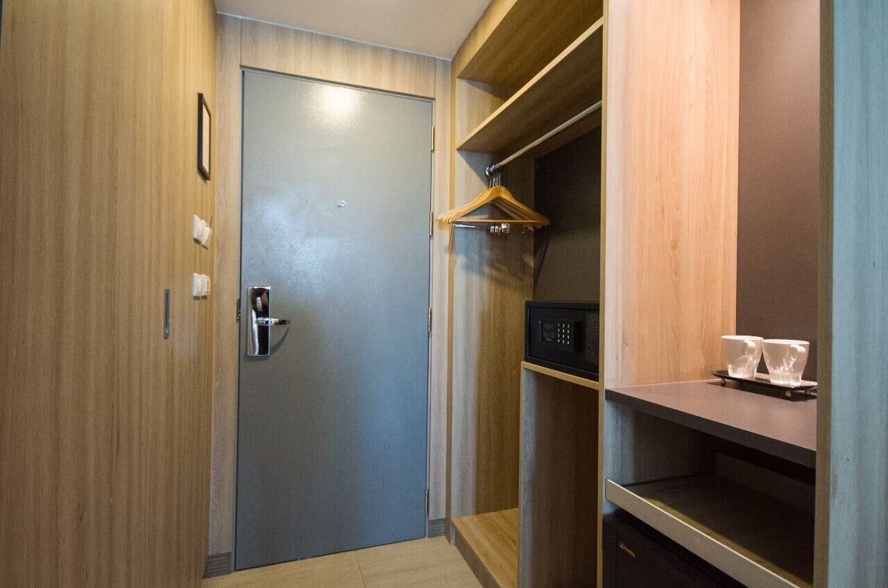 A compact room with a wooden door, a small shelf with a microwave, and a hanging coat rack.