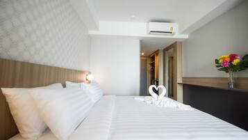 A hotel room with a neatly made bed, a wall-mounted air conditioner, and a vase with flowers on a nightstand.