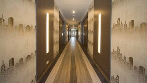Um corredor comprido e estreito, com papel de parede estampado e luminárias verticais em ambos os lados.