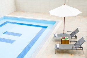 A swimming pool with blue tiles, a white umbrella, and lounge chairs with towels. - Marsi Hotel Bangchak (Bangkok)