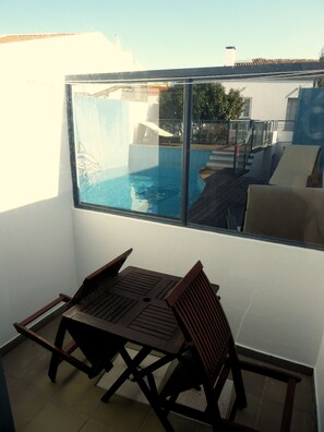Un balcon avec vue sur la piscine, une table en bois et deux chaises.
