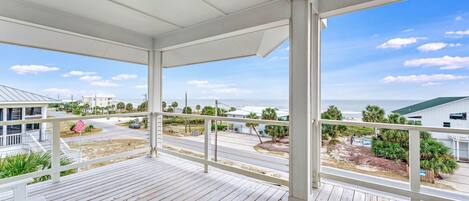 A covered balcony with a view of the beach and neighboring houses.