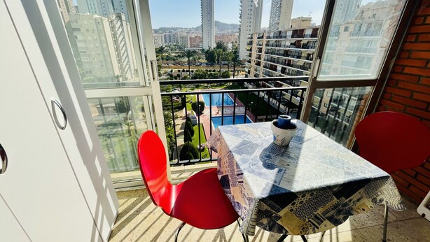 A balcony with a table and chairs, overlooking a cityscape and a swimming pool.