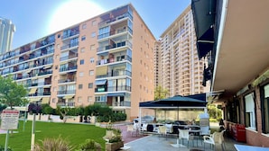 A multi-story residential building with balconies, a patio area with outdoor seating, and a sign indicating pool hours.