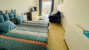 A bedroom with a bed, a desk, a chair, a sofa, and a window with curtains.