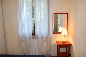 A room with a bed, a bedside table with a lamp, a mirror, and sheer curtains. - Holiday apartment Two room apartment with pool (Lazise)