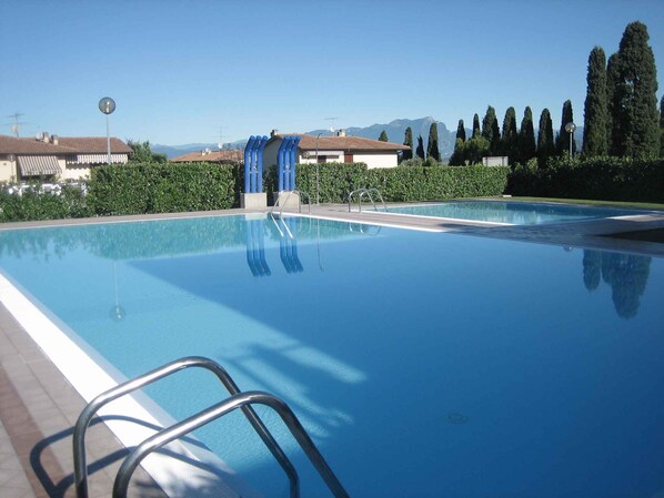 A swimming pool with a clear view of the surrounding landscape, including trees and distant mountains. - Holiday apartment Two room apartment with pool (Lazise)