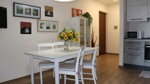 A dining area with a white table and chairs, a vase with sunflowers, and a cabinet with glass doors. - Holiday apartment Two room apartment with pool (Lazise)