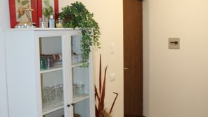 A room with a white cabinet containing glassware and dishes, a potted plant, and a wooden door. - Holiday apartment Two room apartment with pool (Lazise)