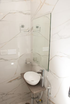 A bathroom with a marble wall, a white sink, a mirror, and a shower.