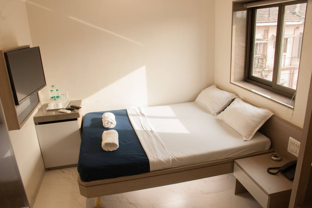 A compact hotel room with a bed, bedside table, and a TV mounted on the wall.