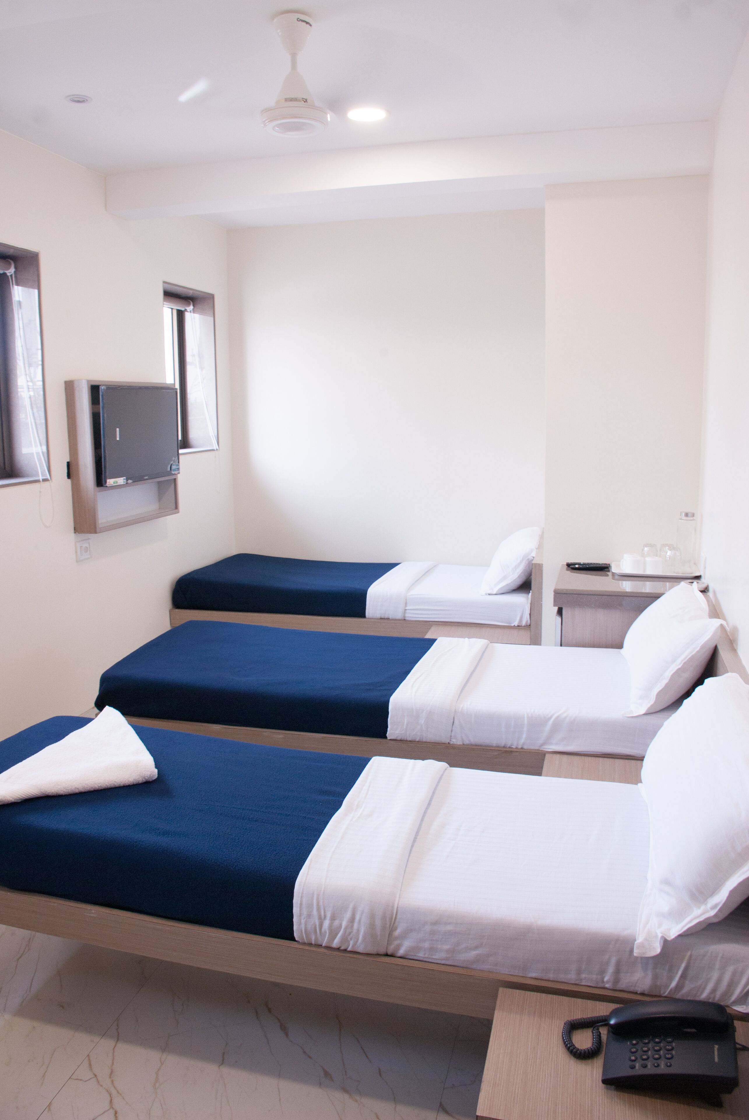 Ein Hotelzimmer mit zwei Einzelbetten, einem an der Wand befestigten Fernseher, einem Nachttisch mit Telefon und einem kleinen Tisch mit Lampe.