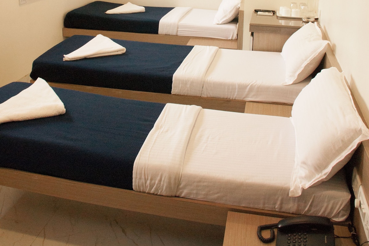 A hotel room with two single beds, a bedside table with a phone, a TV mounted on the wall, and a ceiling fan.