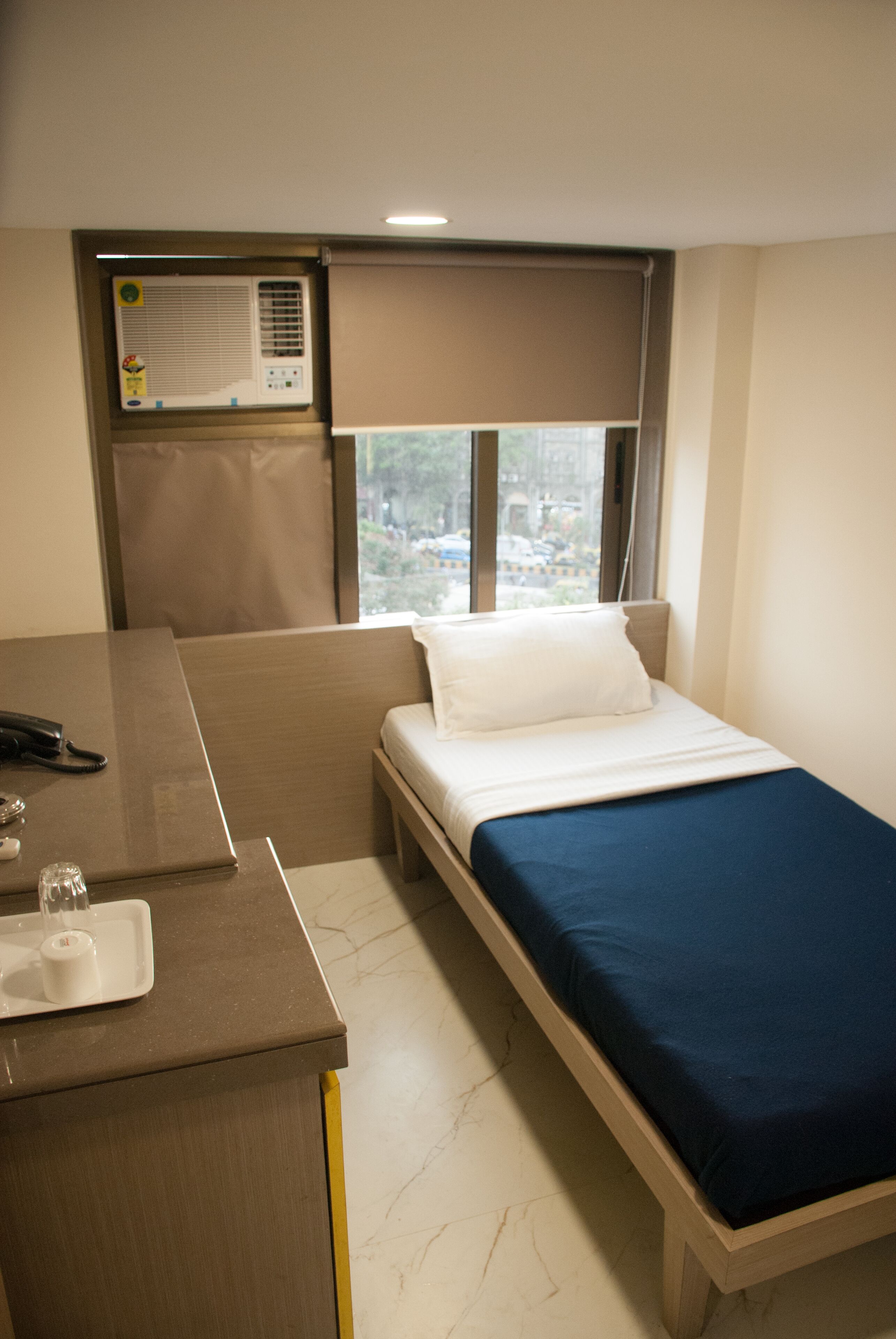 Una habitación de hotel pequeña con cama, escritorio y ventana con vistas a la ciudad.