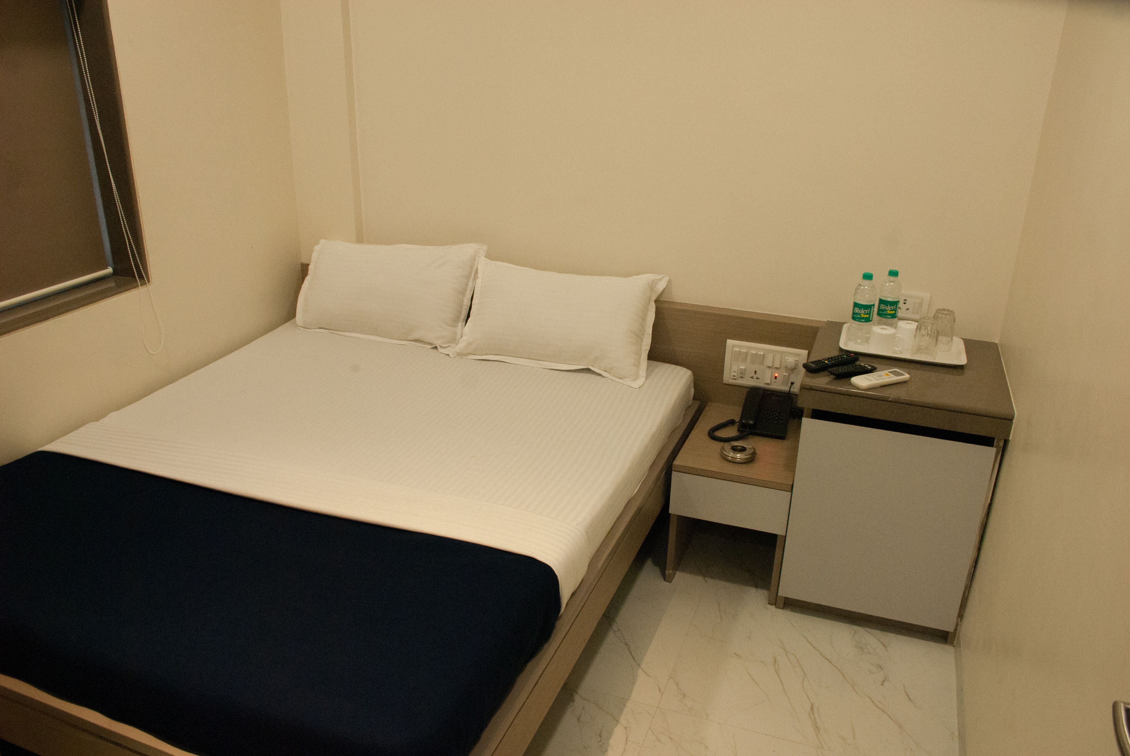 A hotel room with a bed, a nightstand, a small desk, and a mirror.