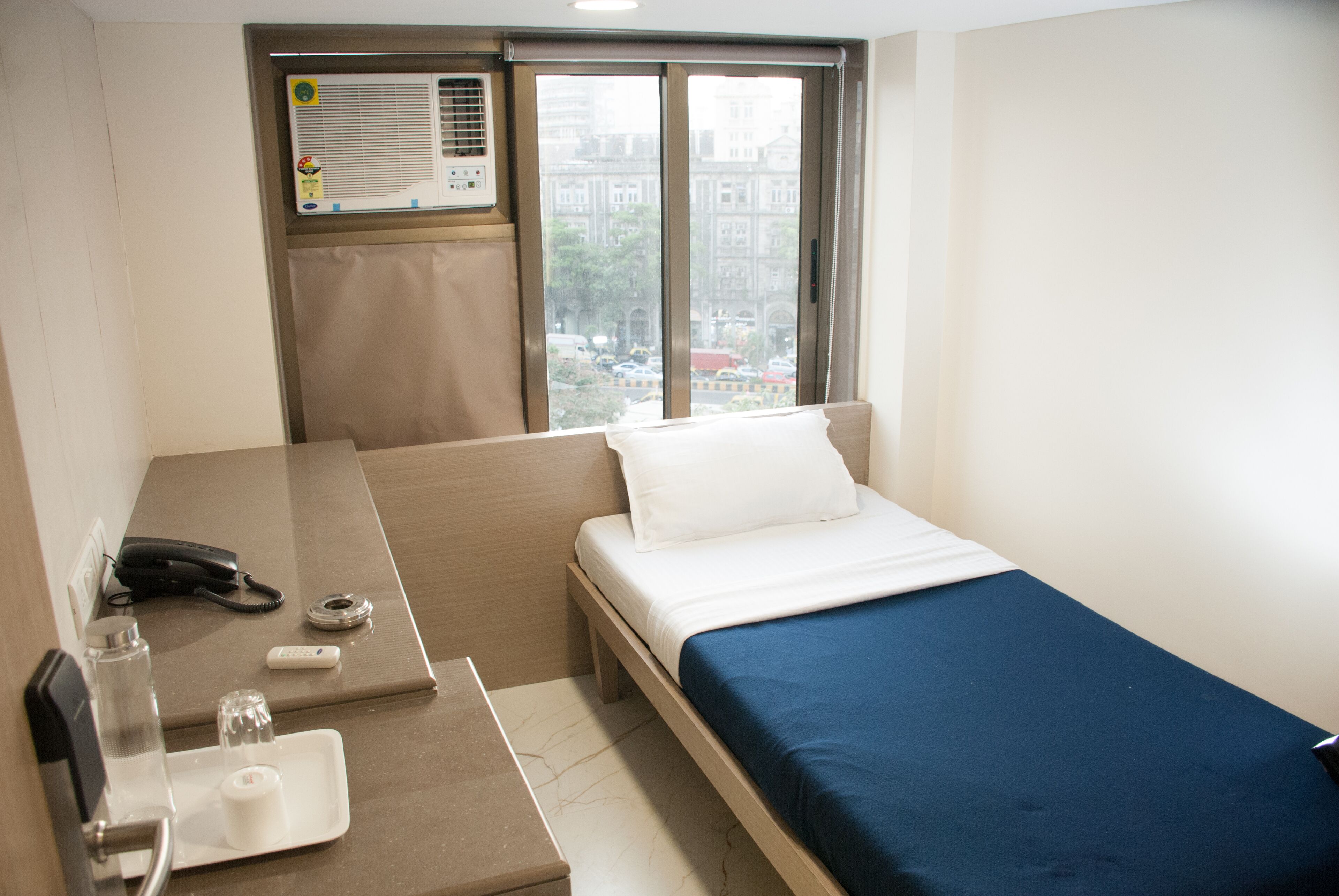 Una habitación de hotel con una cama, un escritorio con teléfono, un control remoto y una ventana con vista a la ciudad.