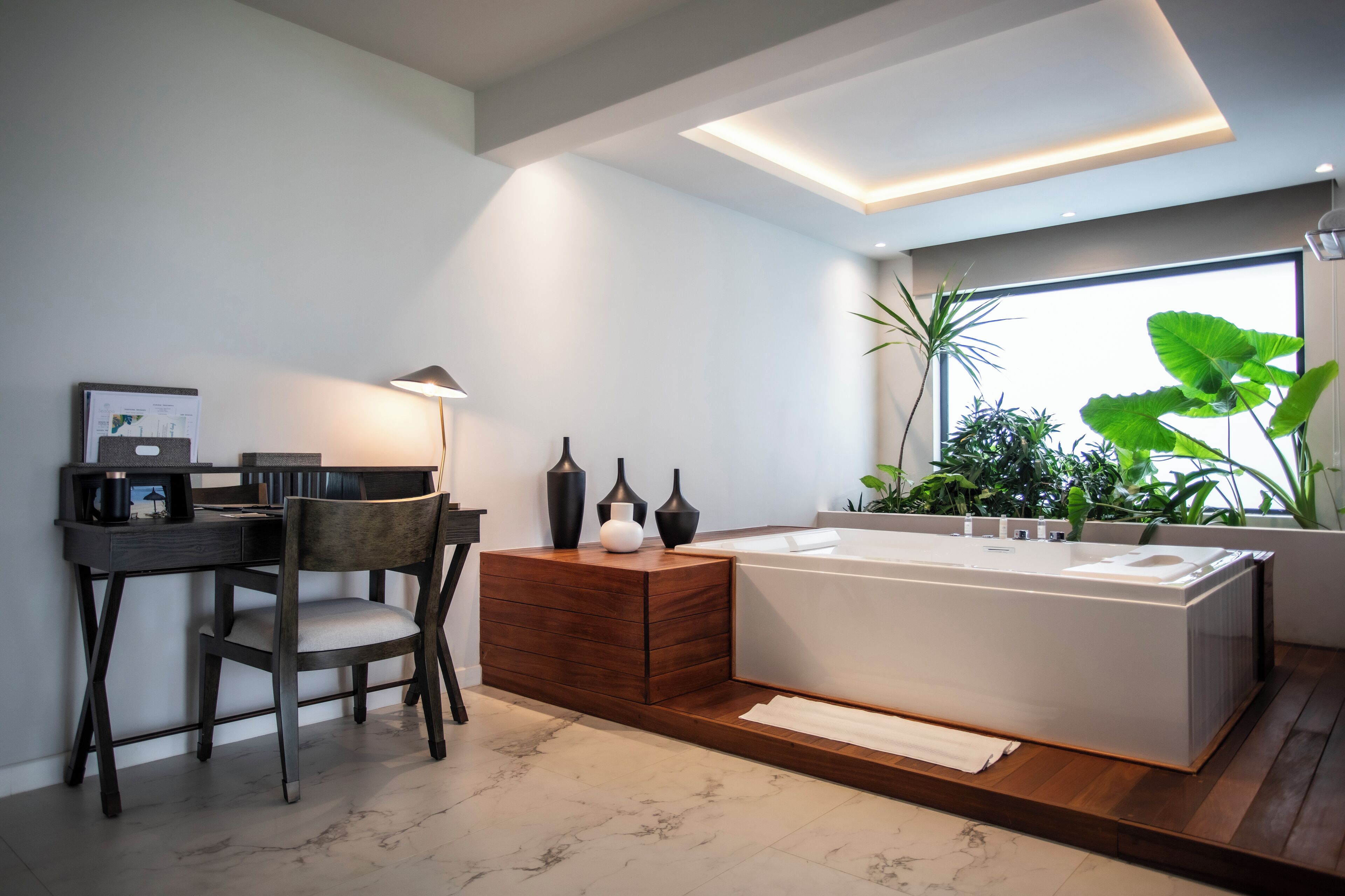 Een moderne badkamer met een ruime badkuip, een houten wastafelmeubel en een bureau met een stoel.