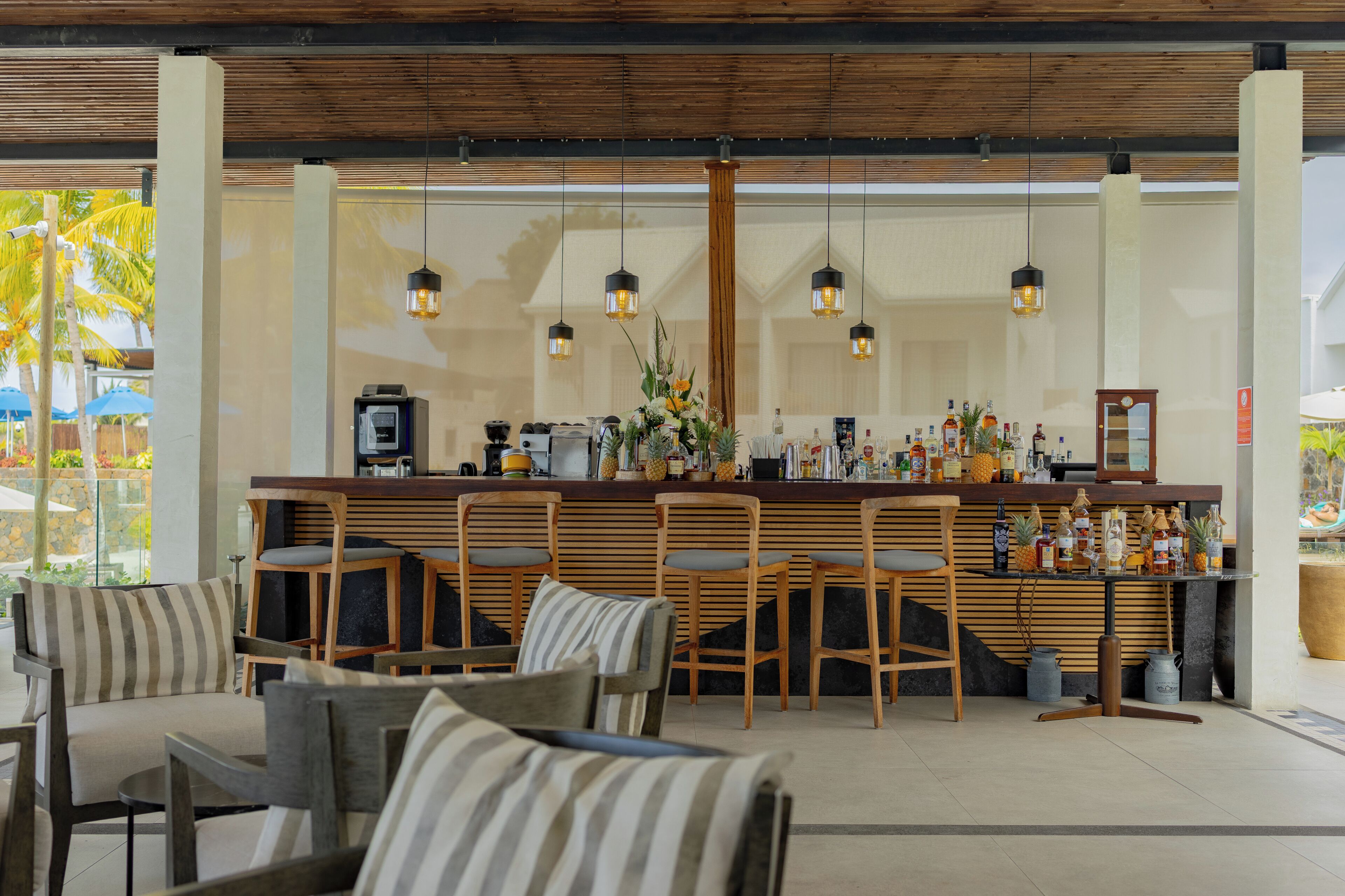 A bar area with wooden chairs, a bar counter with various bottles, and hanging pendant lights.