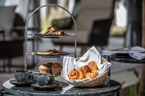 A three-tiered serving tray with pastries and muffins, a basket of croissants, and two cups on a table. - Sea Diamond Boutique Hotel & Spa by Sea Resorts (Calodyne)
