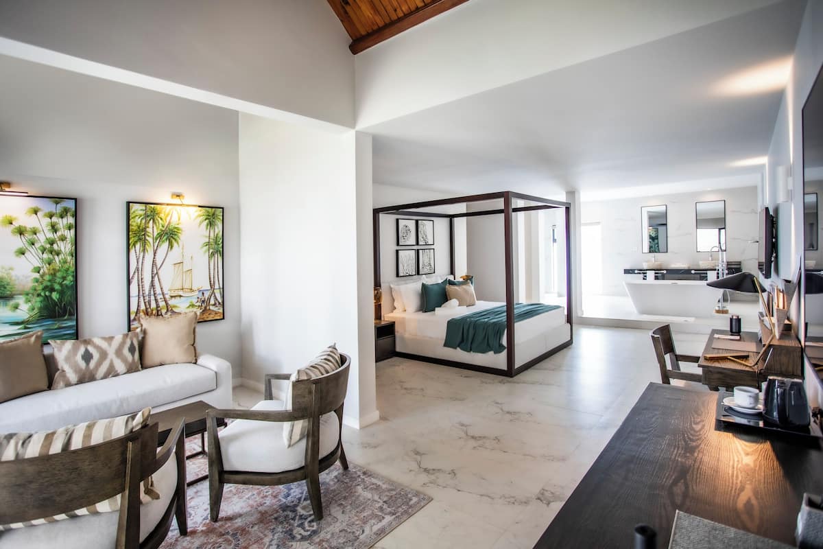 Een moderne hotelkamer met een bank, een eettafel, een bed met hemelbed en kunstwerken aan de muren.