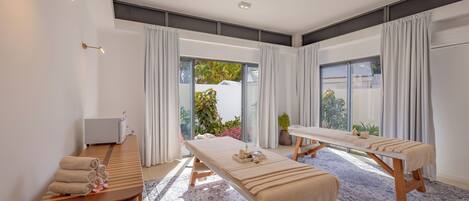 A spa room with two massage tables, a reception desk, and large windows.
