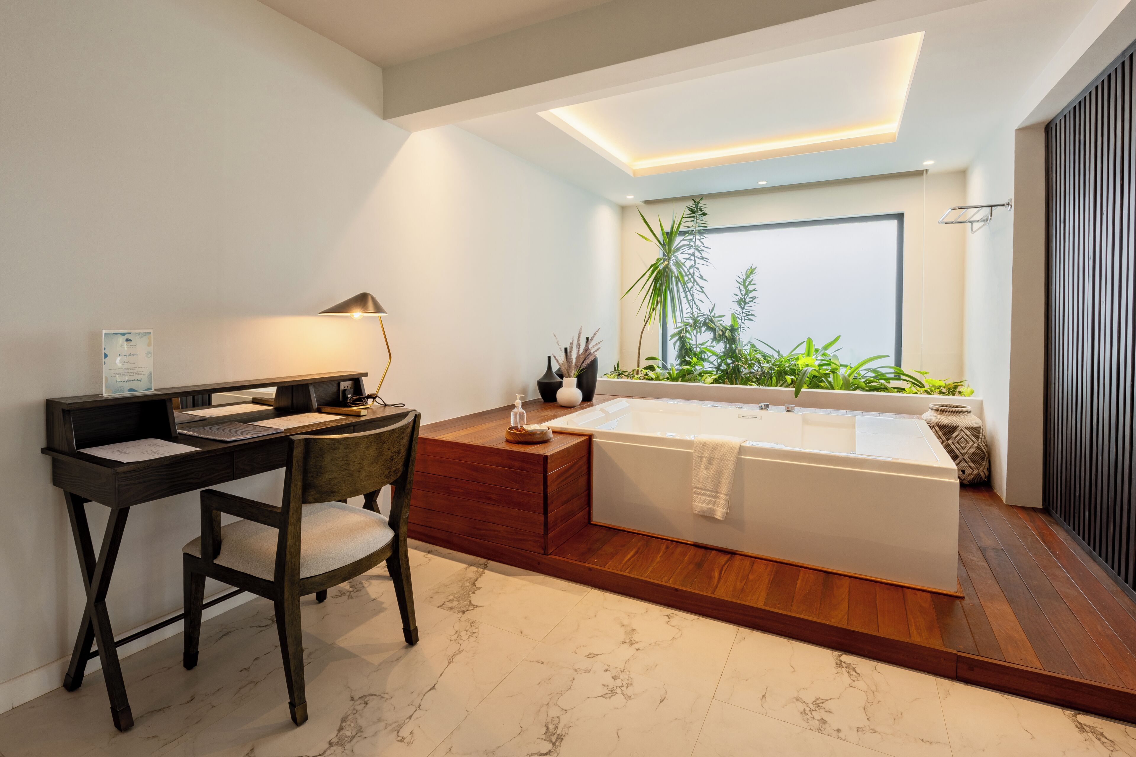 Un baño moderno con tocador de madera, una bañera amplia y un ventanal con plantas.