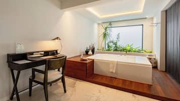 Un baño moderno con tocador de madera, una bañera amplia y un ventanal con plantas.