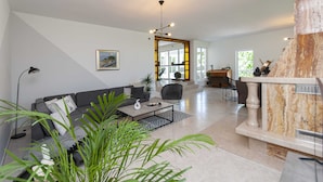 A spacious living area with a sofa, coffee table, and a fireplace. There is a large window providing natural light and a view of the outdoors. - Villa Green Castle (Omis)