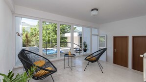 A spacious room with large sliding glass doors leading to a balcony with a pool. There are two black wicker chairs and a small table with a book and a vase. - Villa Green Castle (Omis)