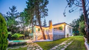 Una casa moderna con un vialetto in pietra che conduce a una piscina, circondata da vegetazione lussureggiante e un cielo sereno.