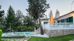 Una casa con facciata in pietra, una piscina e un giardino curato.