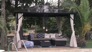 Area piscina con gazebo, un divano con cuscini e piscina.